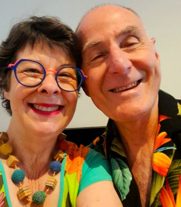 Smiling couple. Woman wearing glasses and chunky necklace. Man wearing Hawaiian shirt.