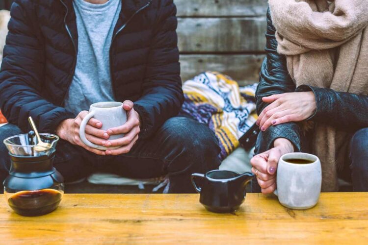 Cropped photo of man and woman sitting at low table drinking hot tea and coffee
